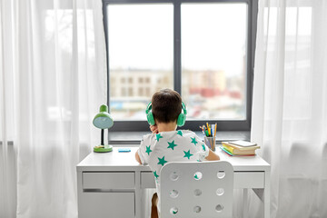 education, technology and school concept - close up of boy in headphones sitting at table at home