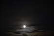 Black background of the night sky. A white fuzzy moon and some bright stars through smoky clouds over a layer of gray clouds.