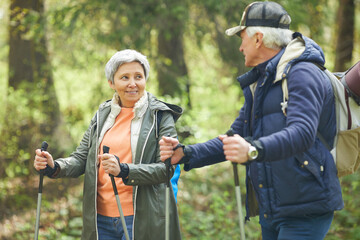 Wall Mural - waist up portrait of active senior couple enjoying nordic walking with poles during hike in forest