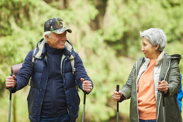 Wall Mural - waist up portrait of cheerful senior couple enjoying nordic walking with poles during hike in forest