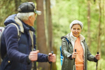 Wall Mural - waist up portrait of active senior woman enjoying nordic walking during hike in forest with husband,