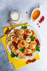 Canvas Print - Mini pancakes with honey, red currant, banana. Yellow runner. White-grey background.  Top view. 