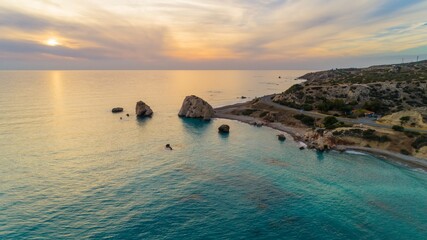 Aerial Bird's eye view of Petra tou Romiou, aka Aphrodite's rock a famous tourist travel destination landmark in Paphos, Cyprus. The sea bay of goddess Afroditi birthplace at sunset from above.