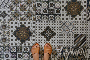 Selfie of feet wearing leather slides on retro ceramics tiles floor 