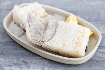 frozen raw cod fish with ice on dish on ceramic background