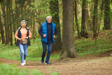 Wall Mural - full length portrait of active senior couple enjoying morning run in beautiful green forest, copy sp