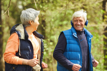 Wall Mural - waist up portrait of active senior couple running in forest lit by sunlight and looking at each othe
