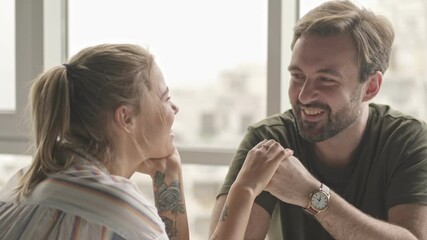 Poster - A smiling young couple man and woman are looking to each other while spending time together sitting at the table at home