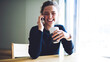 © BullRun - Emotional cute hipster girl laughing during telephone conversation sitting at wooden table indoors.Cheerful young female enjoying tasty coffee while smiling and talking on smartphone with friend