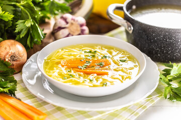 Chicken soup broth in a plate carrot onion celery herbs garlic and fresh vegetables