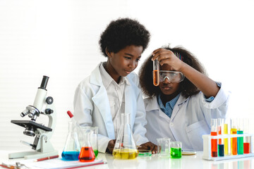 Two african american cute little boy and girl student child learning research and doing a chemical experiment while making analyzing and mixing liquid in test tube at science class on the table