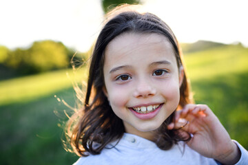 Portrait of small girl standing outdoors in spring nature, looking at camera.