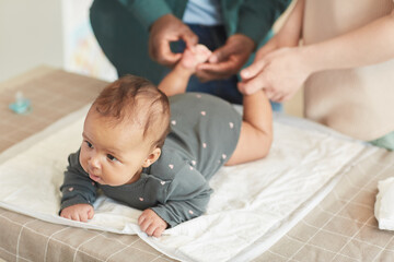 High angle portrait of cute mixed-race baby lying on changing table with unrecognizable parents dressing him, copy space