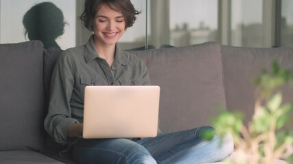 Canvas Print - Cheerful young pretty woman using laptop computer while sitting on sofa at home