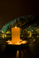 Closeup of candles and flame on the golden tray against cushions and garland lights on the floor