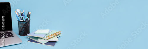 Fotografía Laptop, stack of notepads, stand with stationery on a blue background