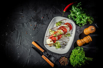 Wall Mural - Caprese salad made of mozzarella cheese, tomatoes and basil leaves on a dark background