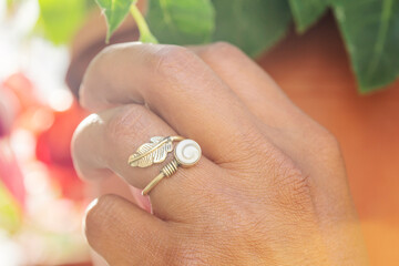 Hand wearing metal ring in the shape of feather, touching the plant