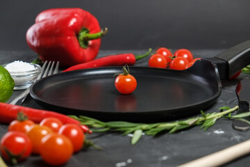 empty round frying pan, fork, fresh rosemary,fresh cherry tomatoes, fresh chilli peppers, garlic, lime and sea salt on black background.