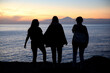 © Belen B Massieu - silhouette of three girls, three young women, at sunset looking at the horizon. Beautiful background. Local travel context, friends' summer trip