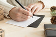 © Snoflinga - Woman writing a christmas card on a wooden table with christmas decoration.
