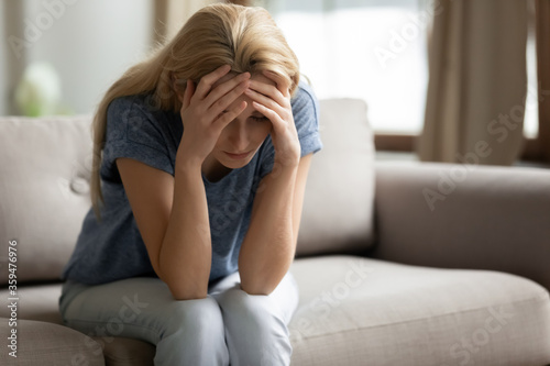 Unhappy young woman suffers sitting on couch alone hold head with hands feels desperate, unwilling pregnancy and abortion decision. Goes through divorce, break up separation with beloved man concept