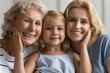 © fizkes - Close up concept image beautiful faces or 3 generations multi-generational relatives women portrait. Little granddaughter pose between old grandmother and young mother family smiling looking at camera
