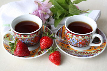 Two cups with coffee, three strawberries and delicate flowers on a white background.