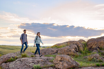 Wall Mural - Young Happy Travelers Hiking with Backpacks on the Rocky Trail at Summer Sunset. Family Travel and Adventure Concept.