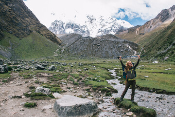 portrait of cheerful female tourist holding trekking stick over head and smiling at camera while sta