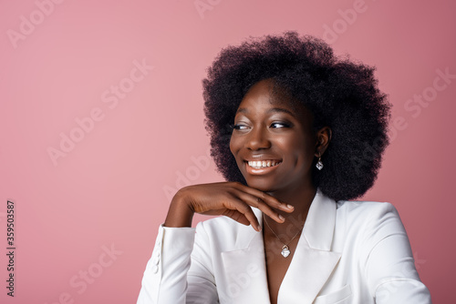Fotografía Yong beautiful happy smiling African American woman, model wearing elegant jewelry, white blazer, looking aside, posing in studio, on pink background