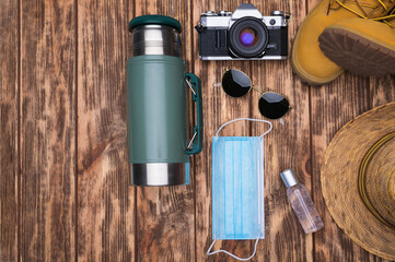 Wall Mural - Travel accessories set on wooden background: face mask, antibacterial gel, hiking leather boots, straw hat, stainless steel thermos and sunglasses. Top view point.