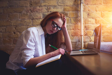 Young female student preparing for university quality control testing writing report analyzing information from internet using laptop computer and wireless connection to internet sitting in library