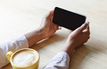 Poster - Cropped view of young woman holding smartphone with blank screen while drinking coffee at cafe, mockup for design