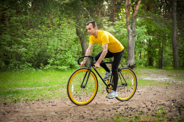 Portrait of a young man moving on a Bicycle. In a public Park, among trees and vegetation.