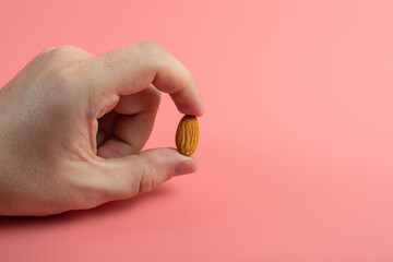 fingers holding almond single almond seed on pink background