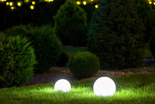 Backyard Ground 2 Light Garden With Lantern Electric Lamp With Sphere Diffuser In Green Grass With Thuja Bushes And Stone Mulching In Park With Landscaping, Closeup Night Scene Nobody.