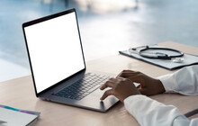 African American Doctor Wear White Coat Typing Using Laptop Computer Mock Up White Screen Browsing Internet Sitting At Work Desk. Healthcare Medical E Health Website Technology Concept. Close Up View