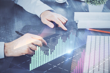 Double exposure of man's hands holding and using a phone and financial graph drawing. Analysis concept.