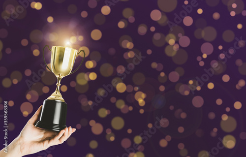 Fotografía Woman holding gold trophy cup on violet background, closeup