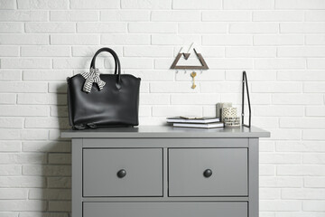 Canvas Print - Grey chest of drawers with bag, books and decor elements near white brick wall