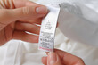 © New Africa - Woman reading clothing label with care symbols and material content on white shirt, closeup