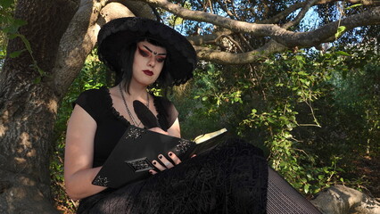 A Wiccan teen wearing a black dress and a witches hat sits in a tree writing in her book. Wiccan and Pagan beliefs are gaining popularity among Generation Z youth.