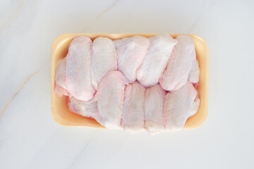 Chilled chicken wings in a yellow tray, fresh meat from the store on a white table. High protein in chicken