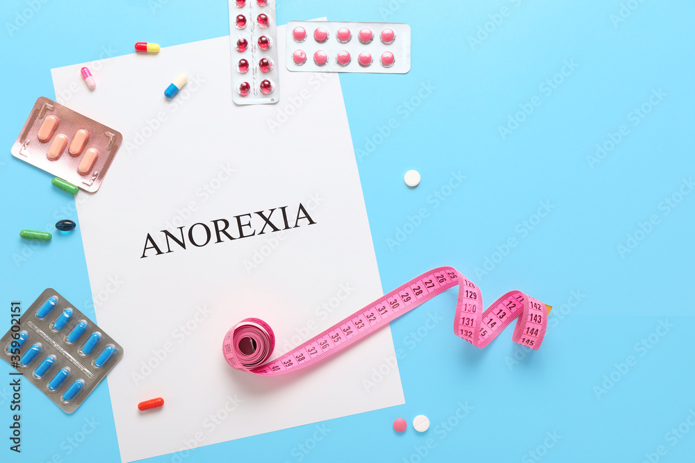 Paper sheet with text ANOREXIA, measuring tape and pills on color background