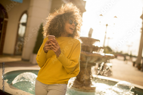 Attractive young woman with curly hair using her touch screen mobile cell phone