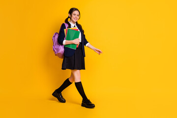 Full length body size view of her she nice attractive pretty cheerful schoolgirl going to secondary school carrying literature isolated on bright vivid shine vibrant yellow color background