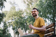 © Oleksii - Young freelancer copywriter wearing stylish eyeglasses, working in park, typing on keyboard. Man using laptop computer, holding cup of coffee, shopping online, sitting on bench