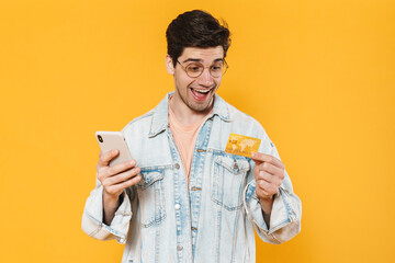 Sticker - Photo of delighted young man holding credit card and using mobile phone