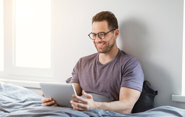 Aufkleber - Happy Man Using Tablet Browsing Internet Sitting In Bed Indoor